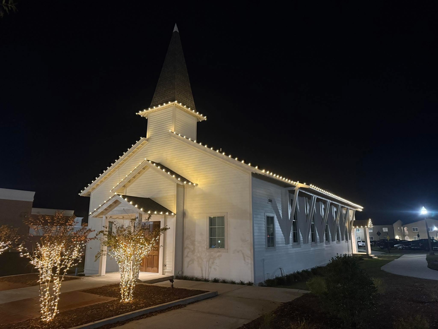 TNT Lighting warm white Christmas light installation on a church with wrapped landscape trees