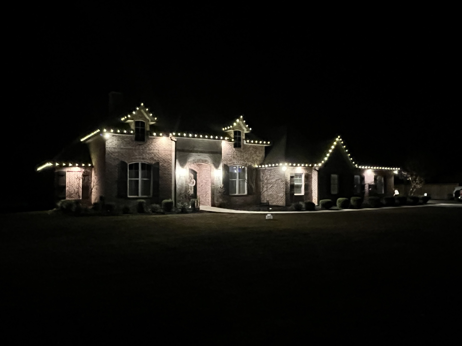 Warm white Christmas lights outlining a large brick property's architectural peaks